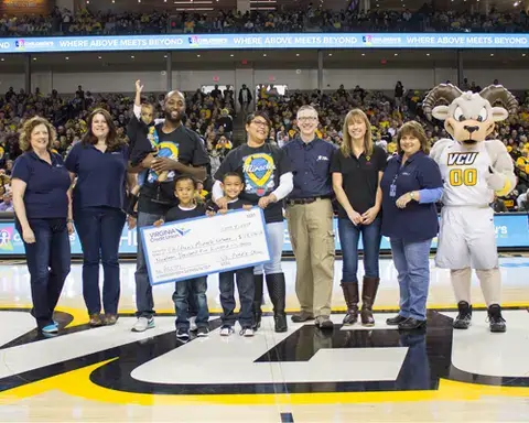 VACU assists holding a giant check with Rodney the Ram at VCU's Segiel Center