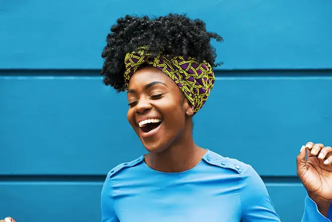 Woman laughs with eyes closed while standing in front of a blue building