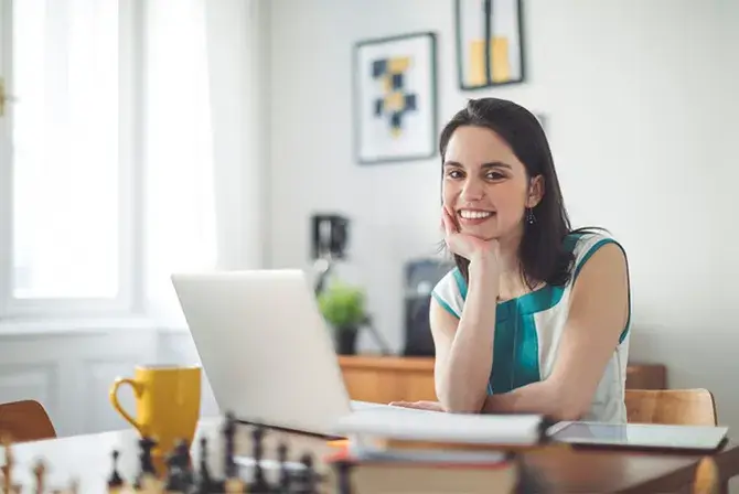 A woman sitting at a table with her laptop open smiling.