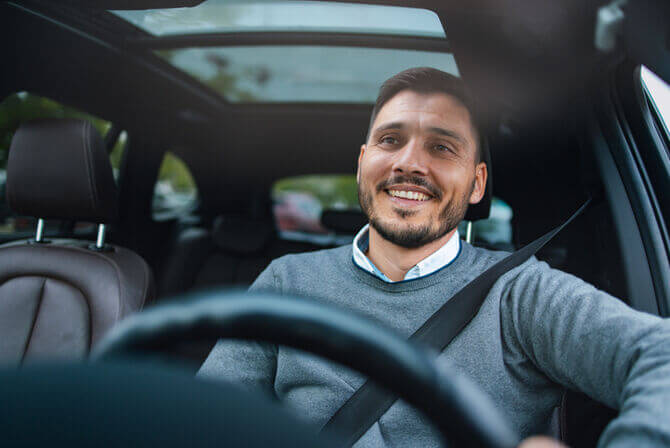 Man sitting in the driver’s seat of a car, smiling as he drives.
