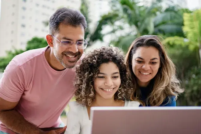 A student and her parents smile as they look at a computer screen