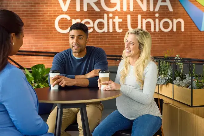 A man and visibly-pregnant woman sit at a table across from a Financial Success advisor in a Virginia Credit Union branch.