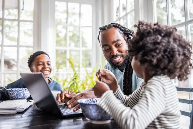 Photo of an African-American father smiling and laughing with his son and daughter at their kitchen table. 
