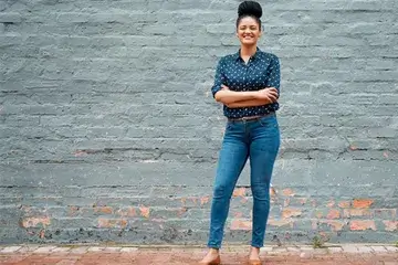 Woman standing outside of a building, smiling with arms crossed