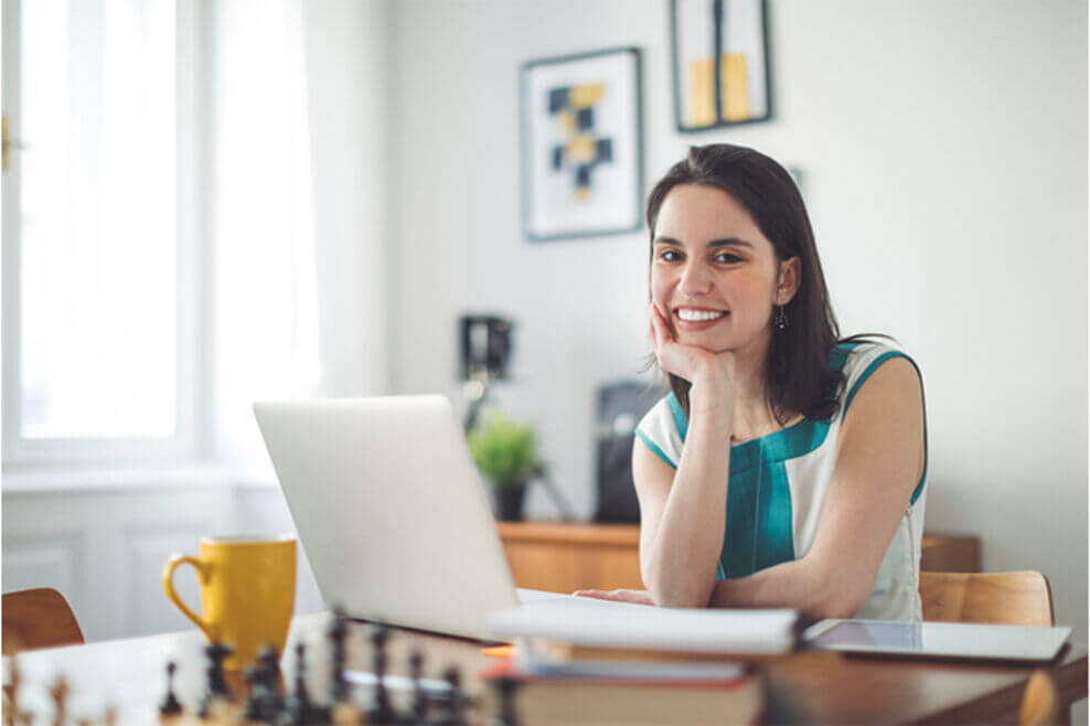 A woman sitting at a table with her laptop open smiling.