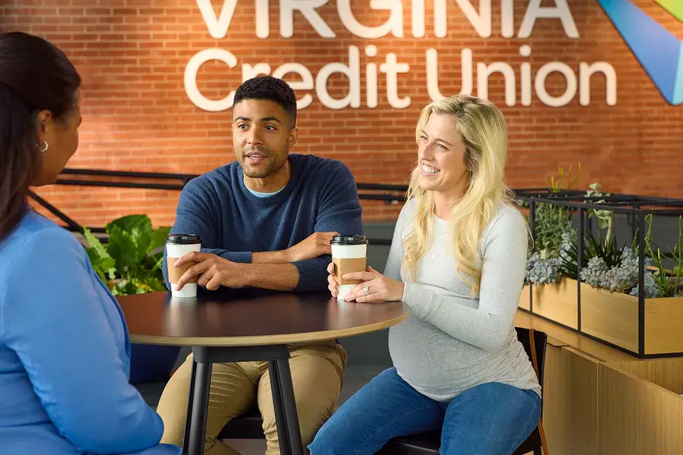 A man and visibly-pregnant woman sit at a table across from a Financial Success advisor in a Virginia Credit Union branch.