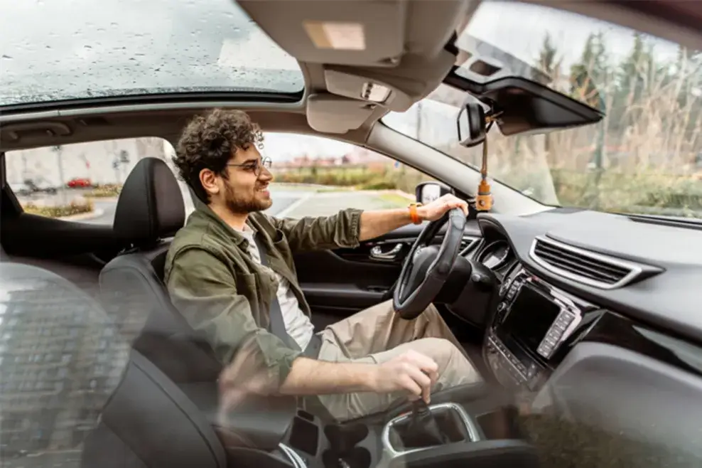 A young man is test-driving a car. He has one hand on the wheel, and the car’s interior features are prominently displayed.
