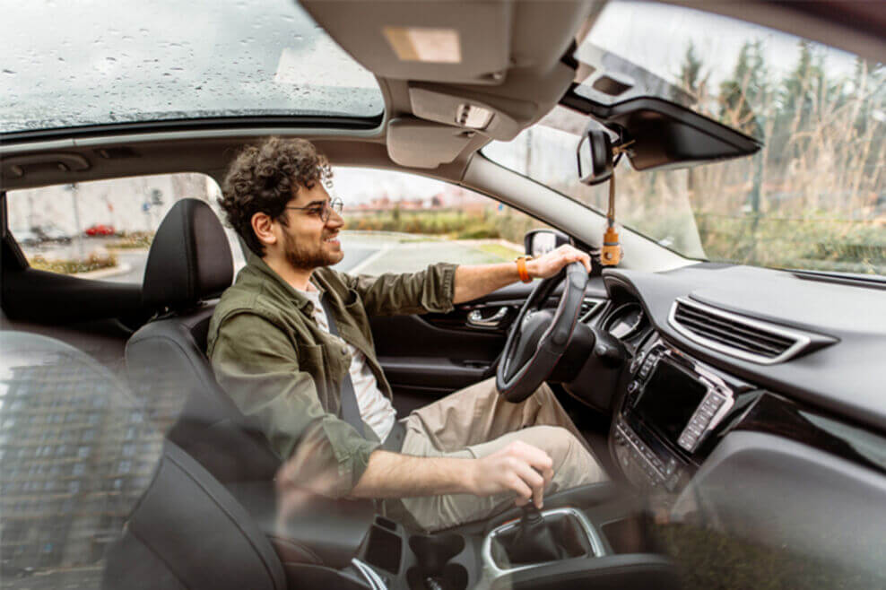 A young man is test-driving a car. He has one hand on the wheel, and the car’s interior features are prominently displayed.