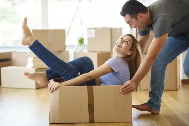 A young couple playfully moving boxes into their new home.