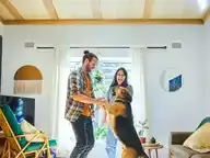 A man and woman dancing and smiling in living room with their dog.