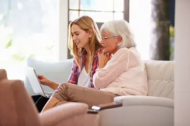 An elderly woman and her daughter sitting on a couch looking at a laptop.