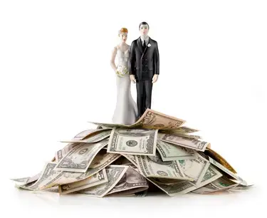 A wedding cake topper of a bride and groom on top of a pile of money.