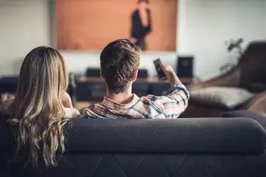 Two people sitting on a living room couch watching the television.