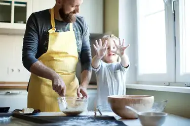 A father and a young child cooking in the kitchen.