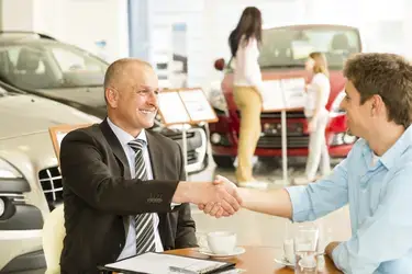 Two men shaking hands inside a car dealership.