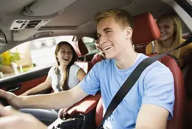A young man driving a car with his friends inside.