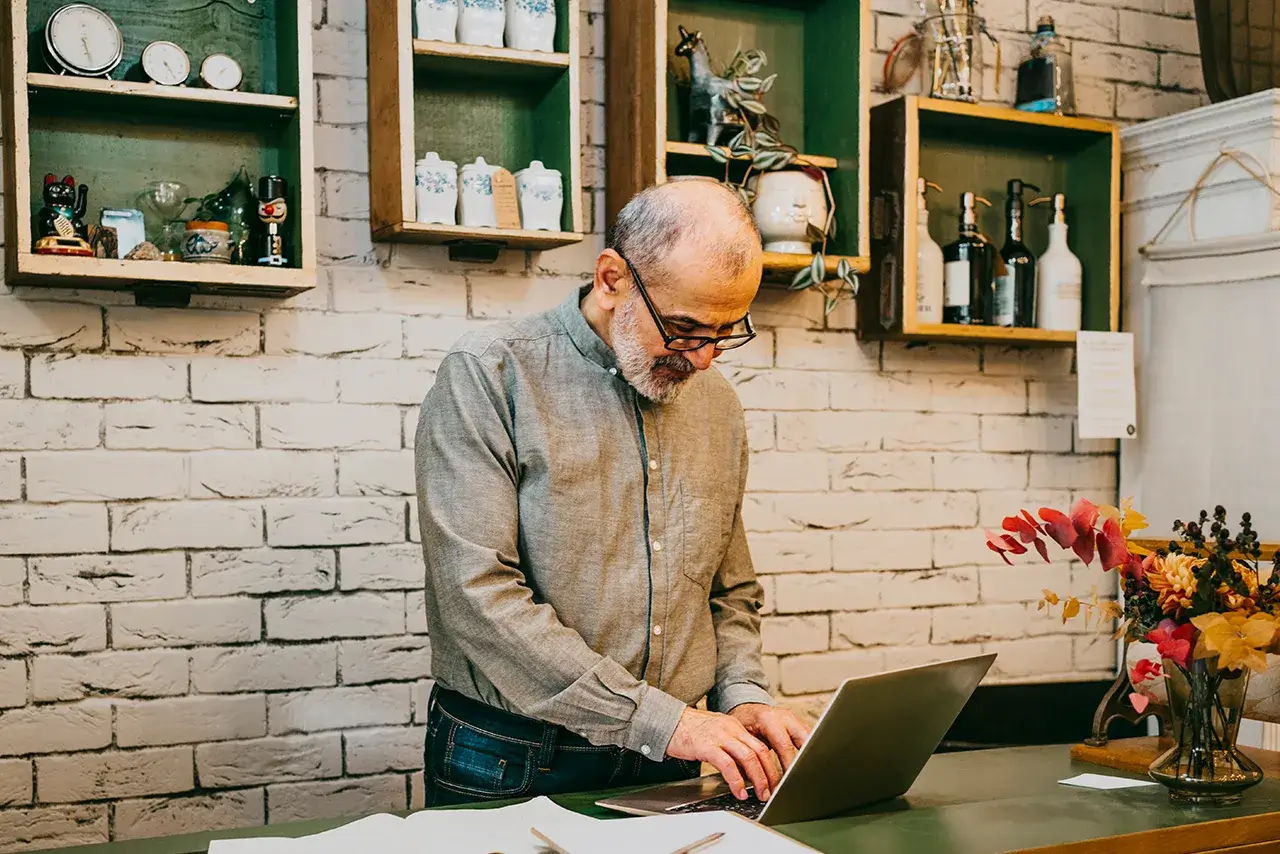 Business owner standing behind a counter with paperwork while typing on a laptop