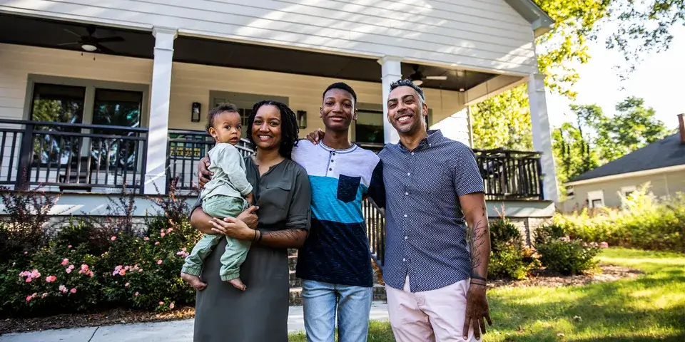 Family of four standing outside of their home, house is seen in the background