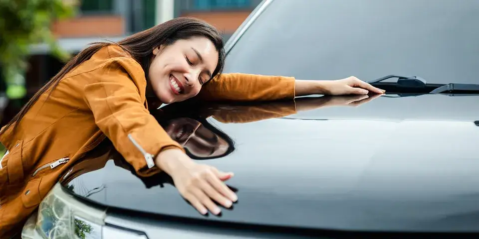 A woman leaning over the hood of a parked car with hands outstretched