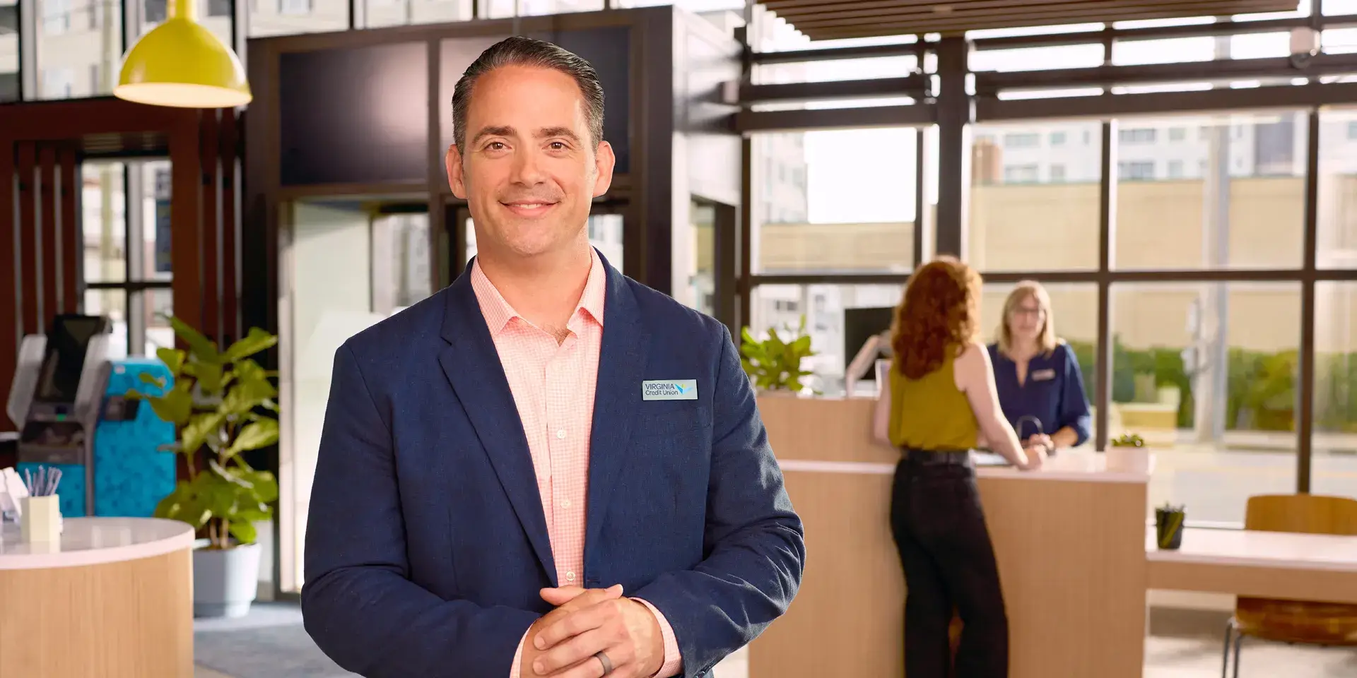 VACU employee smiling while member gets assistance from a teller in the background