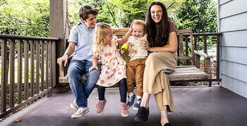 Family of four smiling, sitting together on an outdoor porch swing.