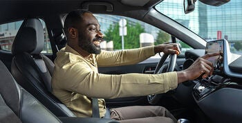 Man smiling, sitting inside car as he is using touchscreen dashboard display.