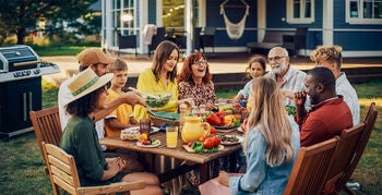 Family and friends gathered around a table in a backyard, with house off in the background