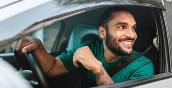Man smiling, sitting behind parked car wheel with window rolled down