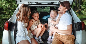 Family of four sit in the back of their parked car with the trunk open