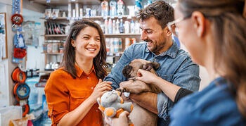 Couple stands in pet store smiling and holding a small dog